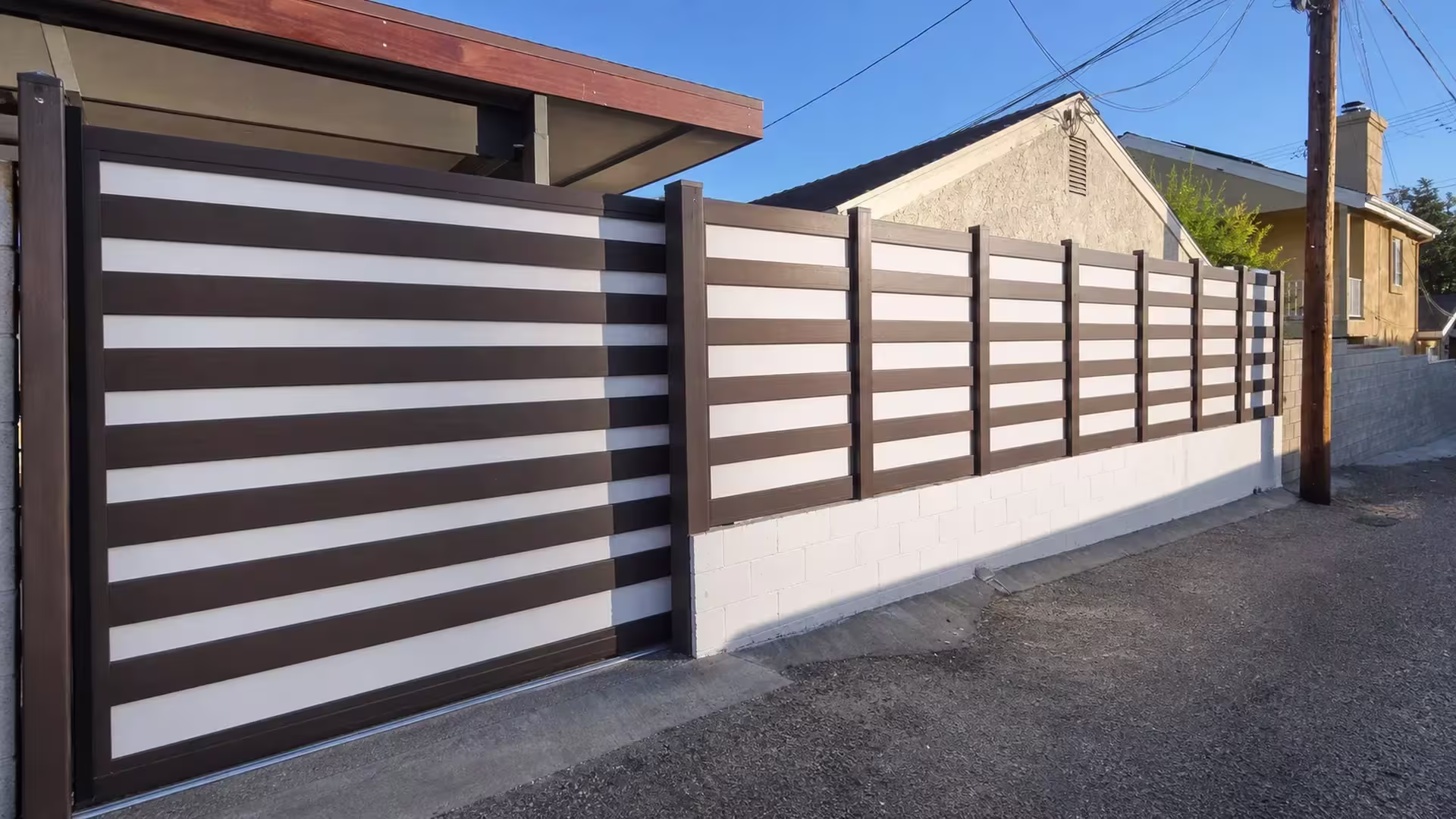 A tan Burbank house with a chimney and balcony rail rises behind a Dark Sequoia vinyl fence with privacy and acrylic panels