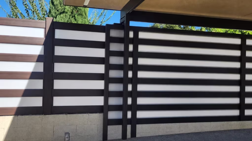 A dark carport's support posts and roof beams frame this Dark Sequoia vinyl privacy-and-acrylic fence in Burbank