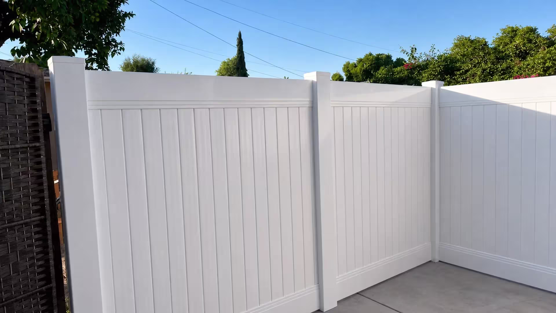 A dark woven boundary screen stands at left of this White vinyl privacy fence forming a right angle corner in Burbank