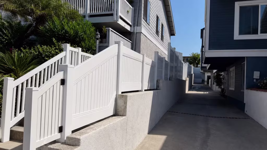 White vinyl picket fence panels step down a masonry wall beside the Redondo Beach driveway stairs
