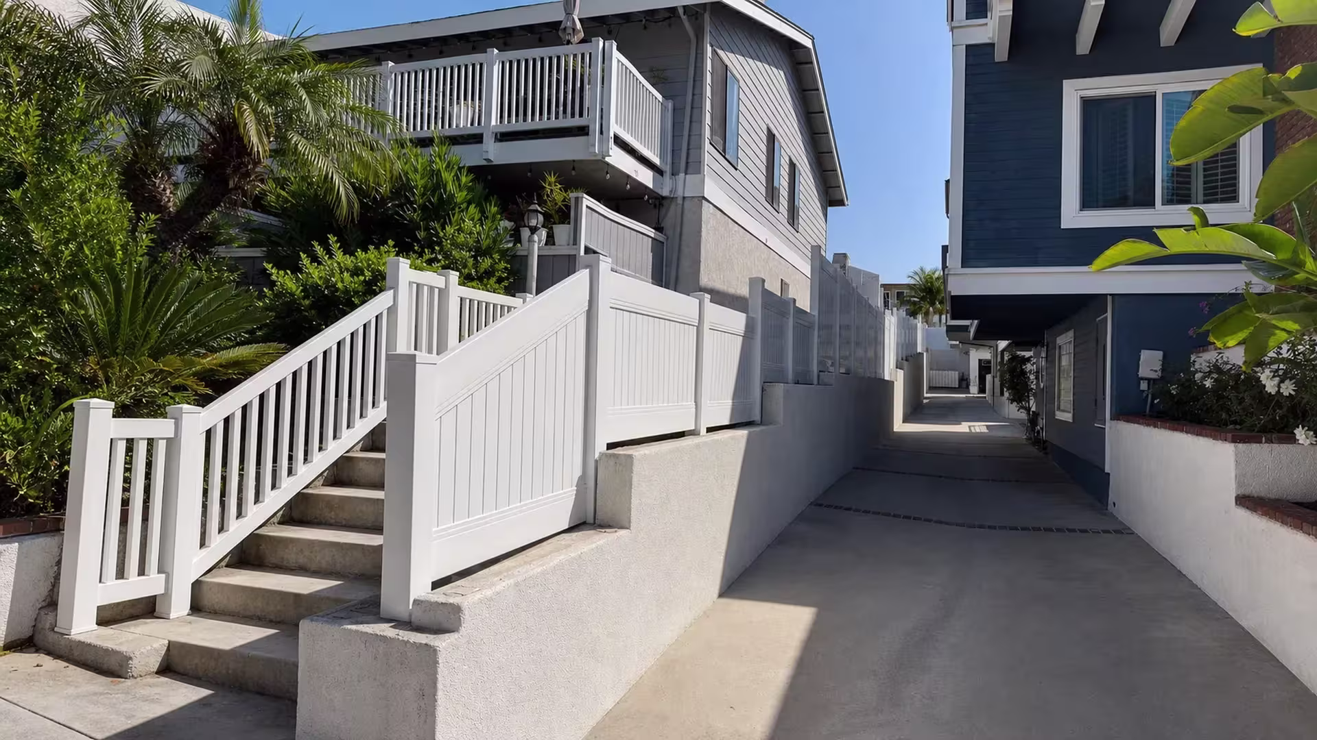 A stucco retaining wall carries a stepped White vertical vinyl picket fence and gate down Redondo Beach stairs