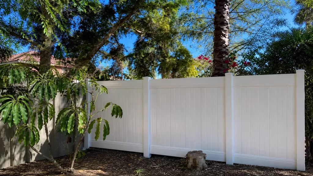 A tall palm trunk and a sparse planting bed sit behind this White vinyl fence in a Granada Hills yard