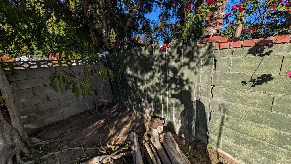 Before installation, a dark green wood gate stands between aging green block walls amid exposed roots and broken wood debris.
