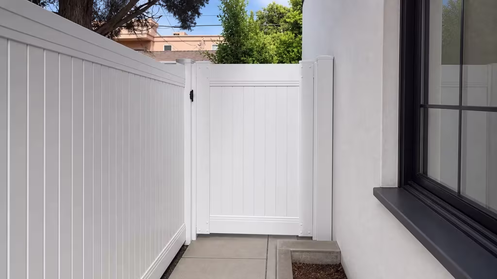 A peach building next door stands close to this White vinyl privacy fence along a Los Angeles side walkway