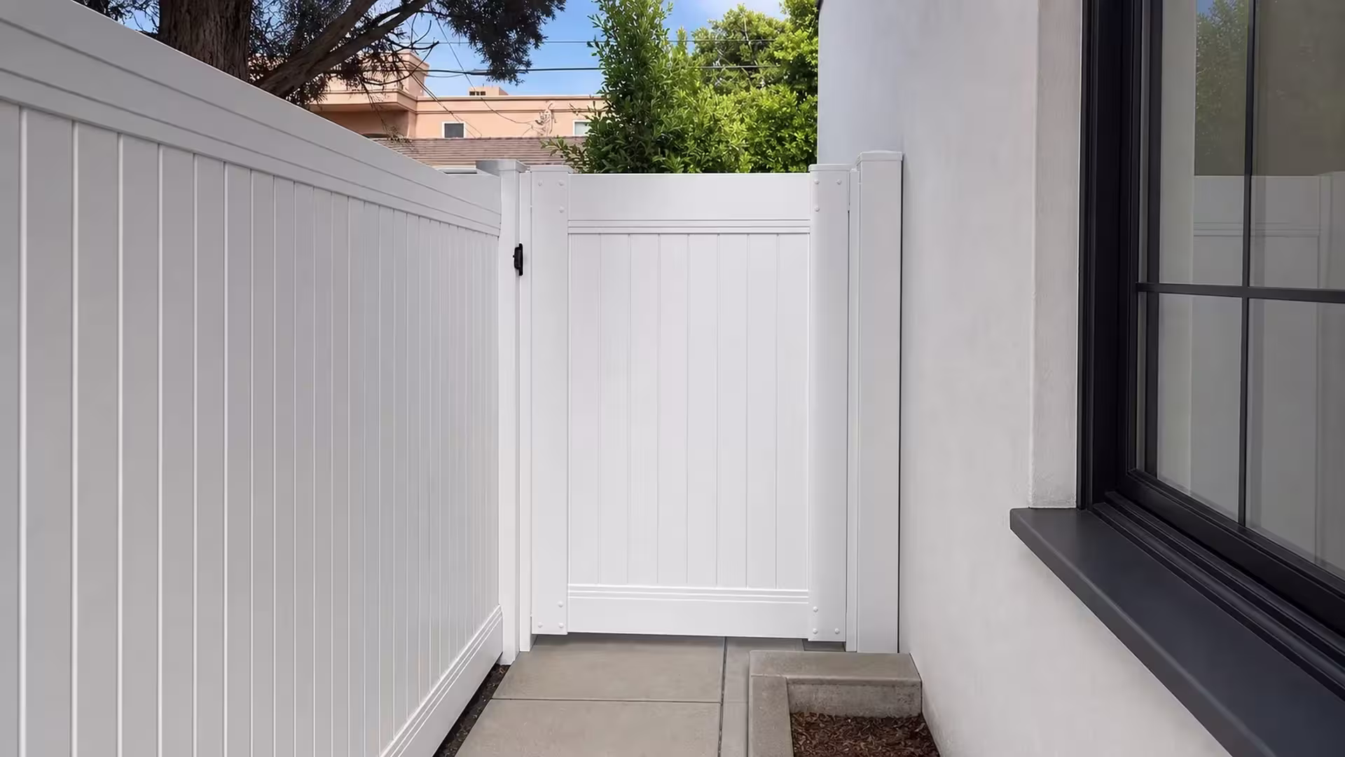 A peach building next door stands close to this White vinyl privacy fence along a Los Angeles side walkway