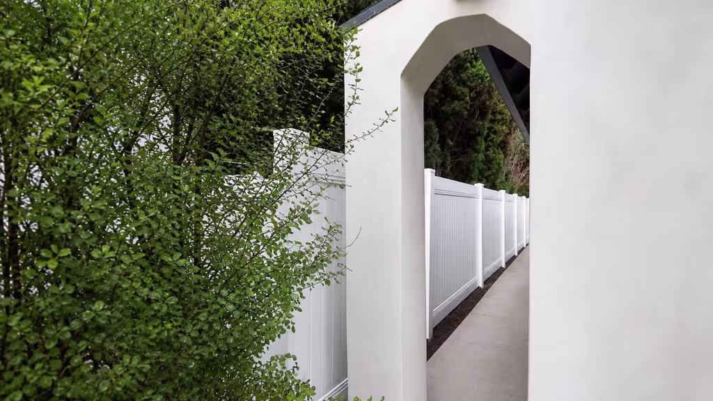 A stucco arch and columns rise behind this White vinyl privacy fence angling along a narrow Los Angeles walkway