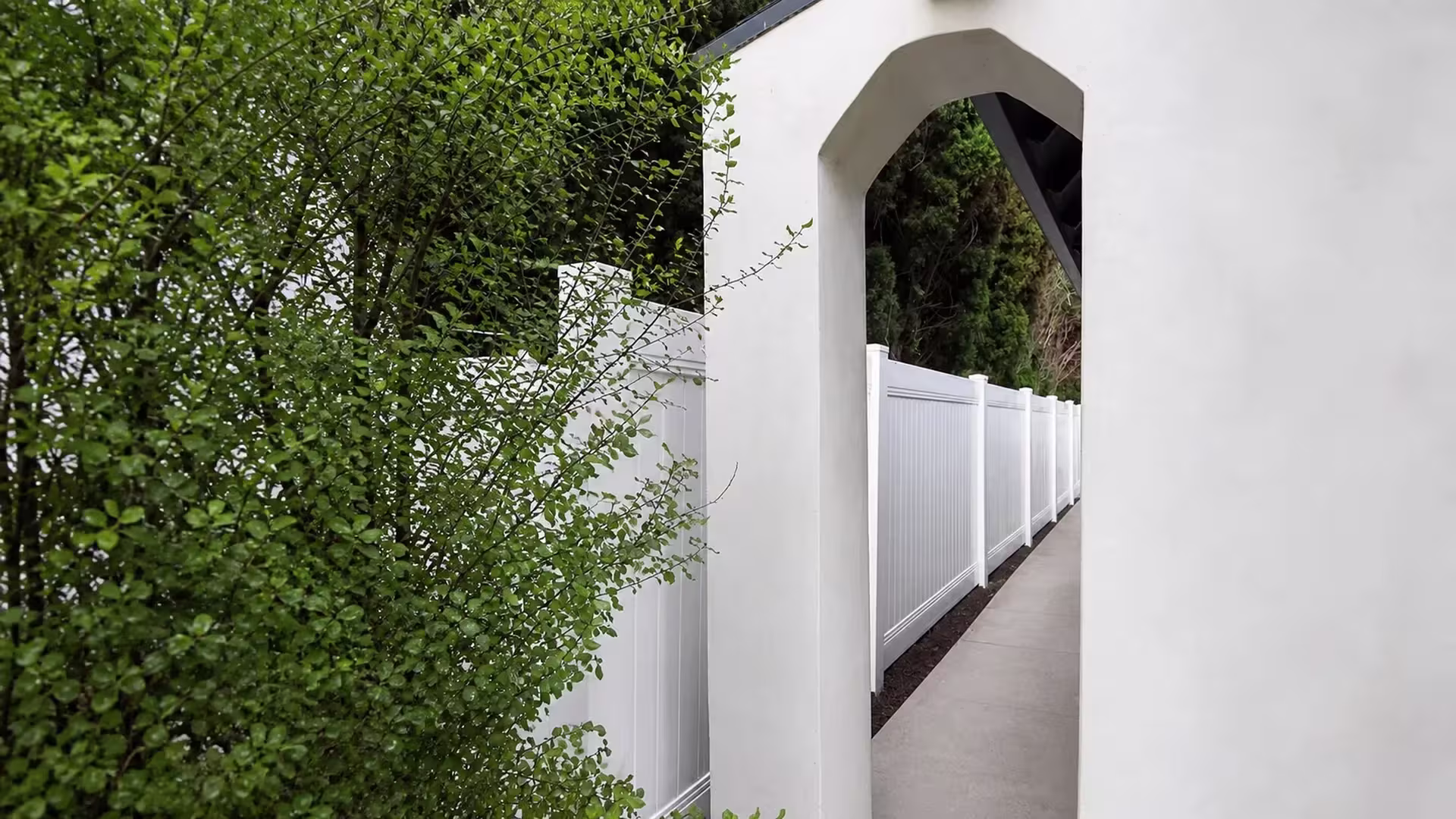 A stucco arch and columns rise behind this White vinyl privacy fence angling along a narrow Los Angeles walkway