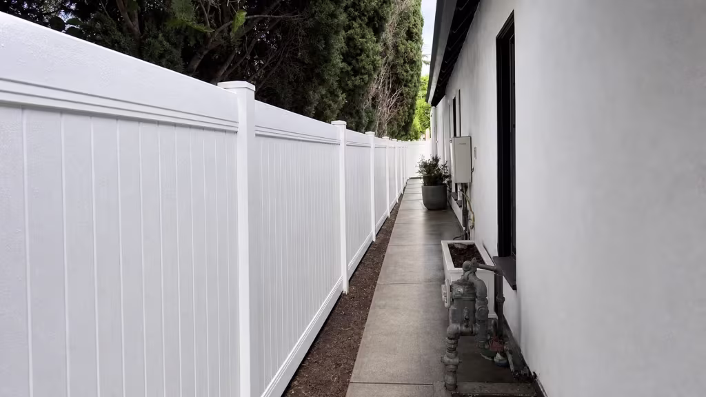 A gas meter and regulator assembly sit beside this White vinyl privacy fence lining a Los Angeles walkway
