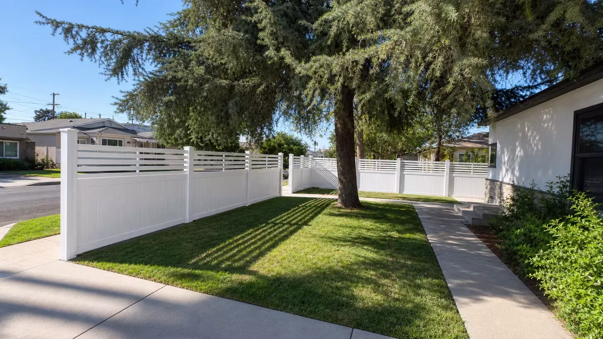 Aspen vinyl privacy fence encloses the front yard, its horizontal picket top rising above stone veneer and a mature conifer