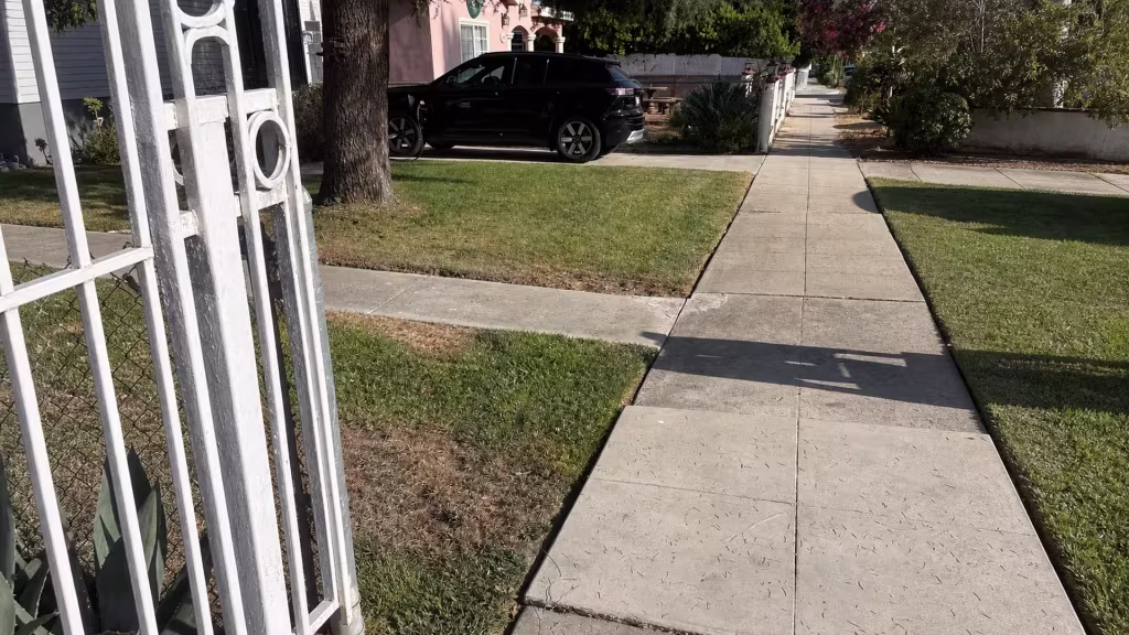 Before installation, an open white metal gate stands at a front walkway beside a lawn and sidewalk.