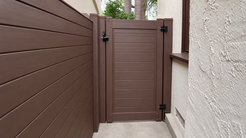 A brown-trimmed window and palms overlook this narrow Los Angeles passage, closed by a Dark Sequoia vinyl fence and gate
