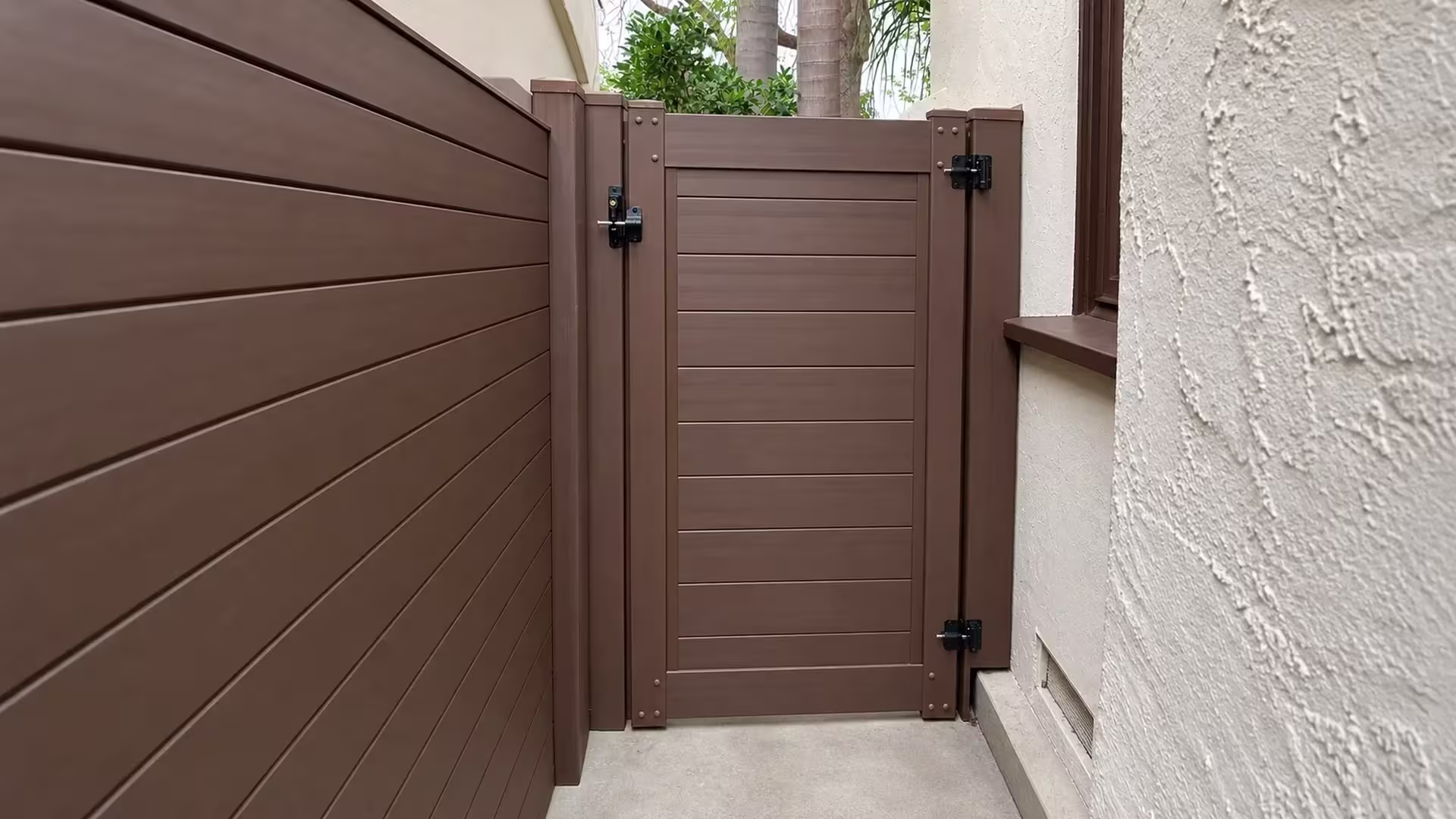 A brown-trimmed window and palms overlook this narrow Los Angeles passage, closed by a Dark Sequoia vinyl fence and gate