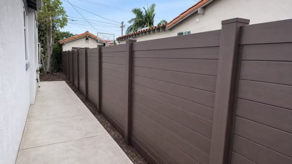 Dark Sequoia vinyl privacy fence and gate lining a narrow side yard past a basketball backboard in Los Angeles