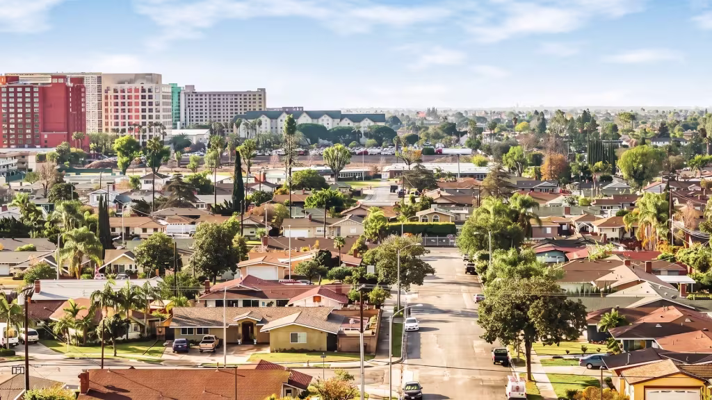 A broad residential street in La Mirada leads toward a low-rise center with mountains beyond