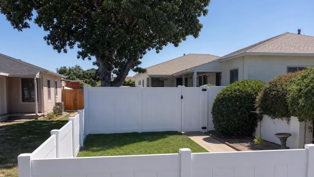A mature tree and a planted hedge stand behind this White vinyl privacy fence crossing a Los Angeles backyard