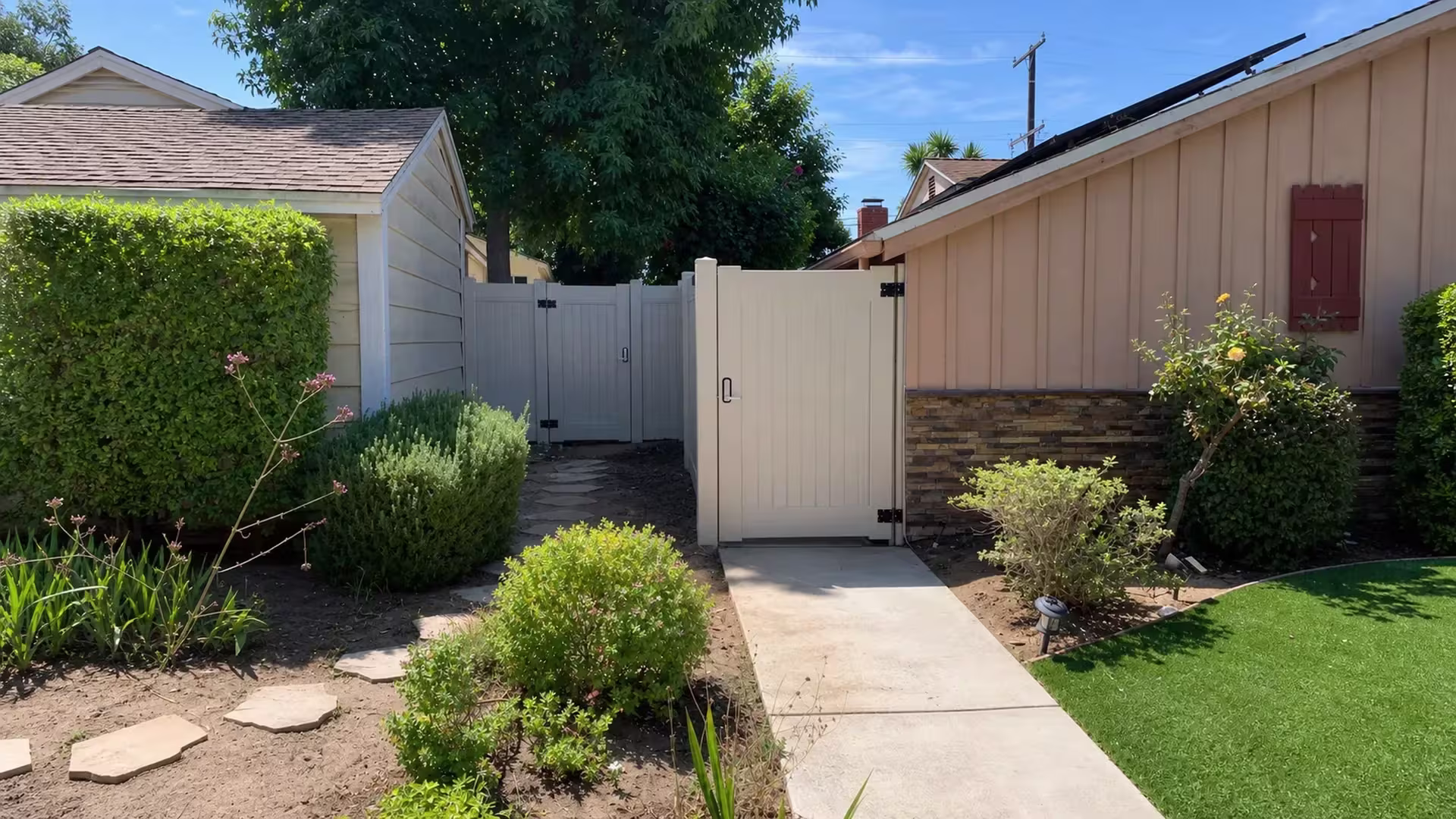Tan vinyl pedestrian gate with black hinges set into the privacy fence along a narrow Culver City side yard
