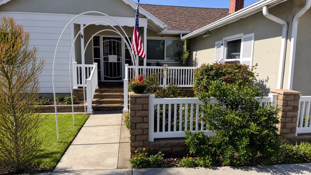 A flagpole and garden arches stand near this White vertical vinyl picket fence, where its railing crosses a Long Beach porch