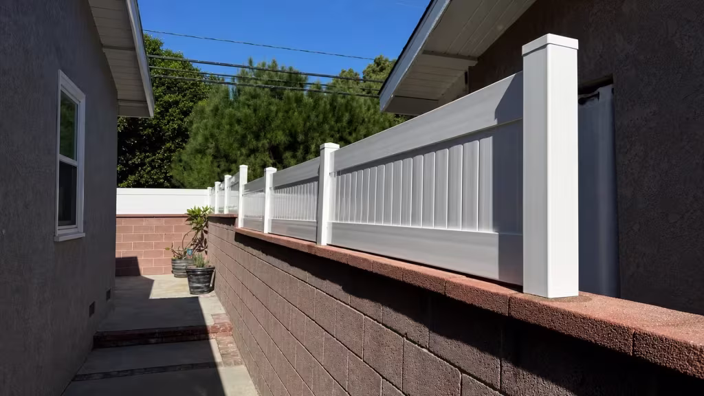 A red-brown capped block wall carries a White vertical vinyl picket fence near a Long Beach walkway