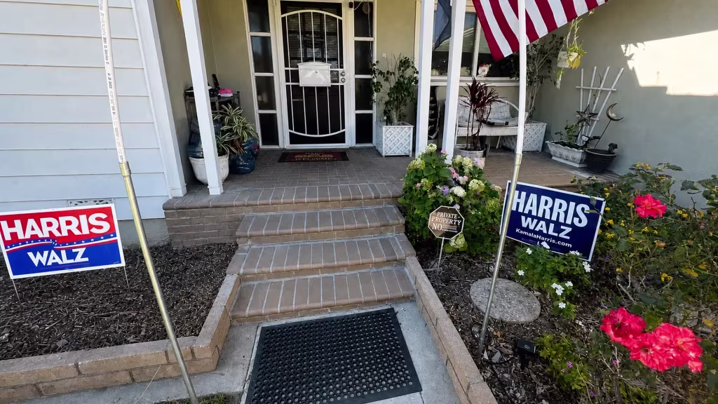 Before installation, a brick front porch and steps are surrounded by flowering plants and small garden signs.