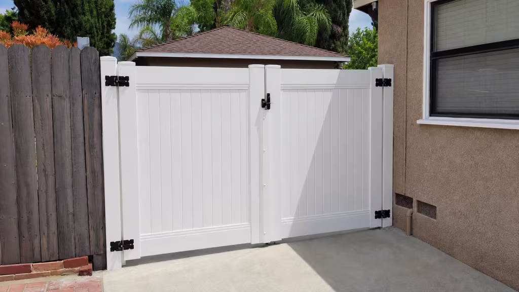 A screened window and trim break up the stucco wall beside a White vinyl privacy double gate in Shadow Hills