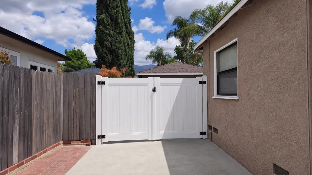 White vinyl privacy double gate framed by a shingled outbuilding roof and distant mountains
