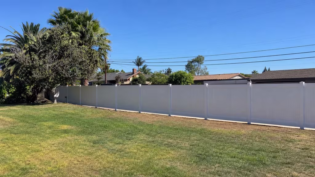 Clustered palms and a broadleaf tree stand at the left of this White vinyl fence lining a Rancho Palos Verdes lawn