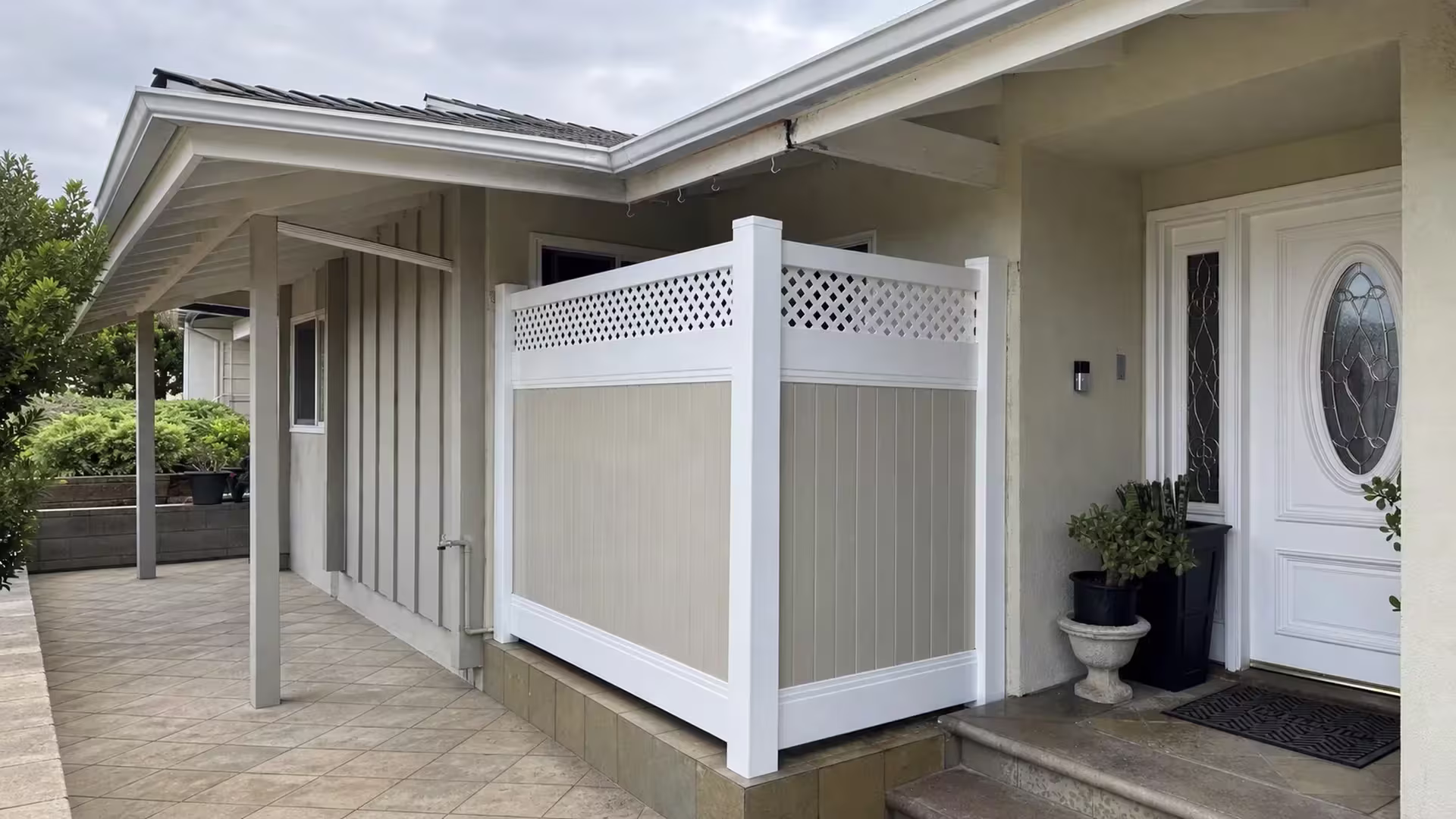 A black planter and a stone pedestal planter with succulents sit beside this Tan and White vinyl fence in Glendale