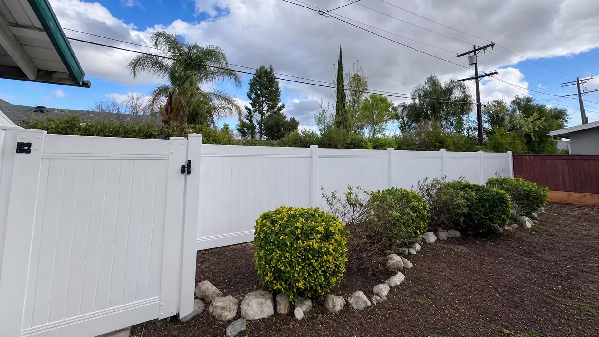A yellow-green round bush and a stone border sit beside this White vinyl privacy fence in West Hills