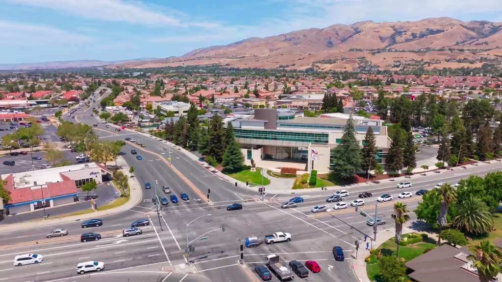 A broad road intersection splits residential districts and dry hills across Milpitas