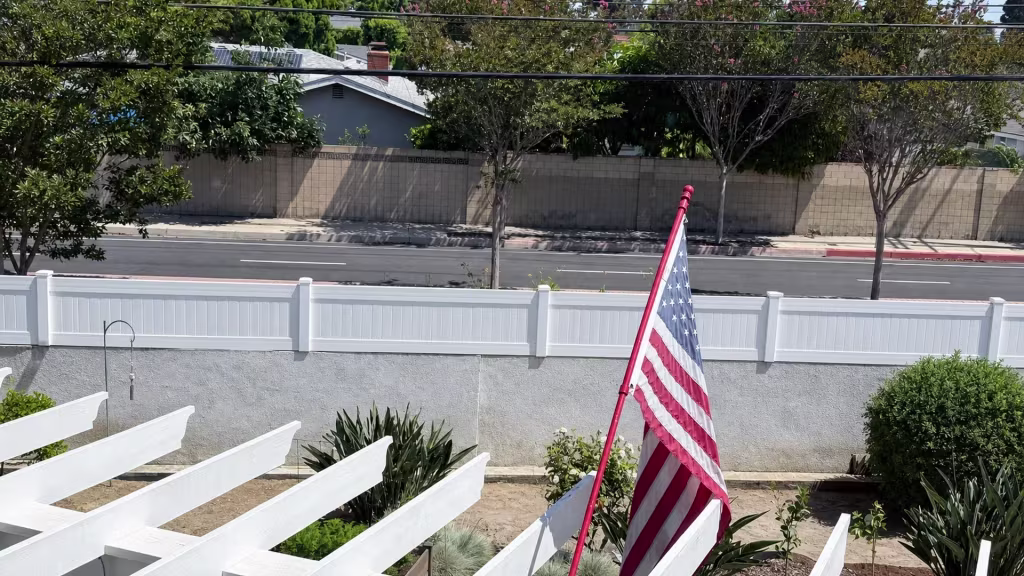 White vinyl privacy wall topper facing a yard where a large American flag flies on a red pole