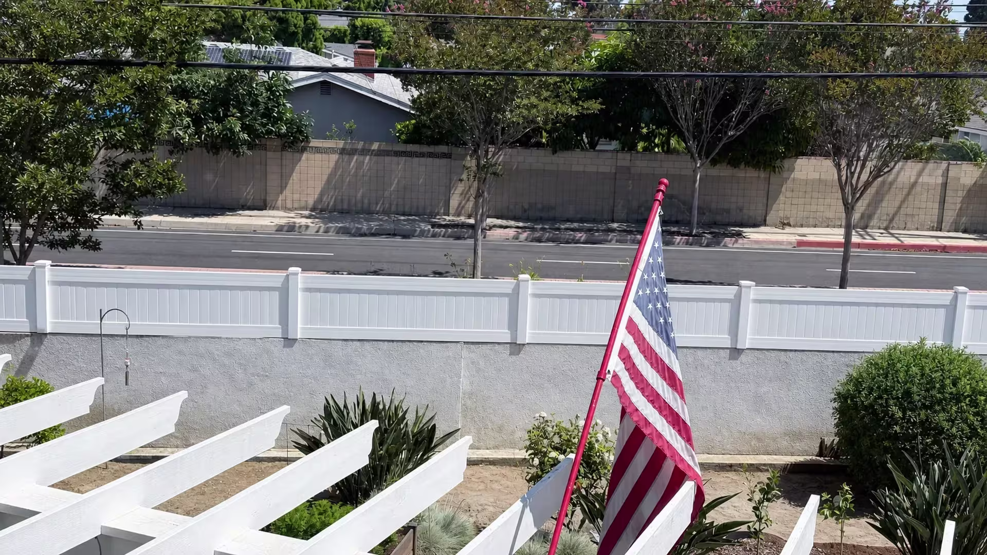 White vinyl privacy wall topper facing a yard where a large American flag flies on a red pole
