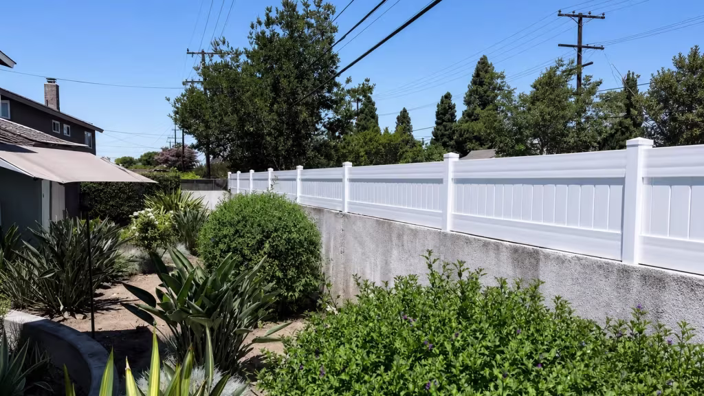 Succulents and flowering plants border the neighboring building beside a White vinyl privacy wall topper here