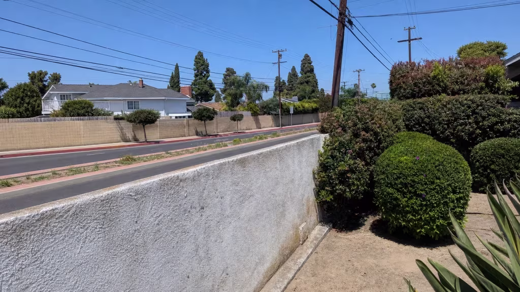 Before installation, a low white stucco wall borders a landscaped front yard overlooking the street.
