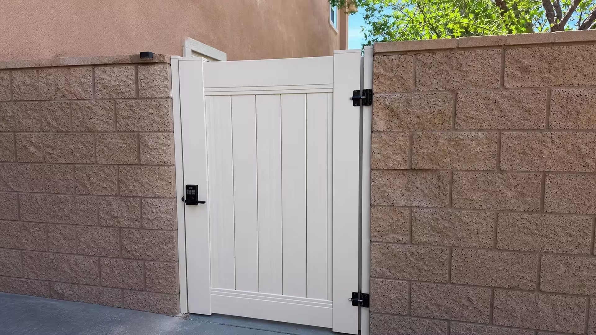 A white-trimmed window looks over the stucco wall behind this Tan vinyl privacy gate in a Los Angeles side passage