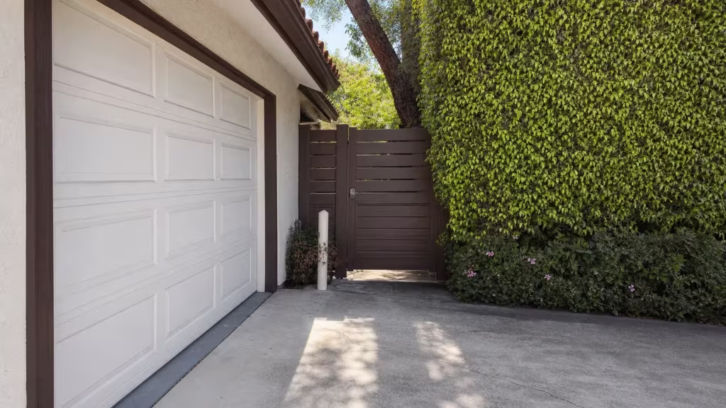 Clay tile roofline and a mature tree stand behind a Dark Walnut picket top vinyl privacy gate near a Los Angeles hedge