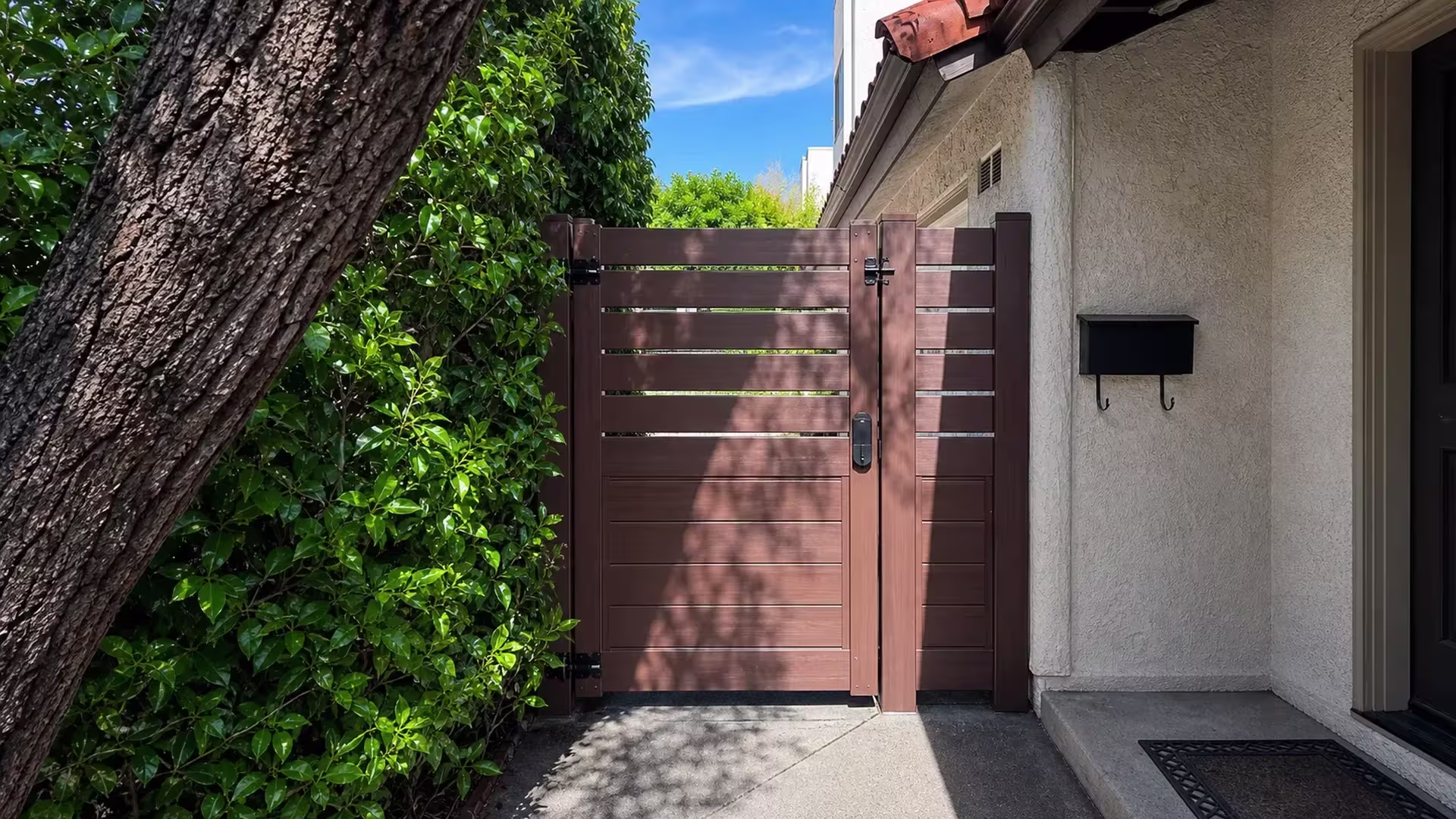 Dark Walnut vinyl gate with a picket top closing a side passage beside a stucco house wall