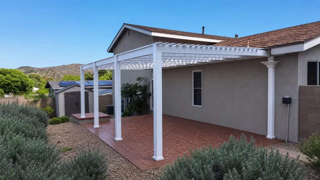 Rooftop solar panels show above the open lattice roof of this White vinyl pergola patio cover against a gray stucco wall