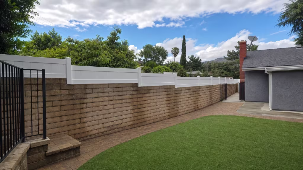 Mountain and palm silhouettes rise past a gate ending this Sunland property's White vinyl wall topper, kept for privacy