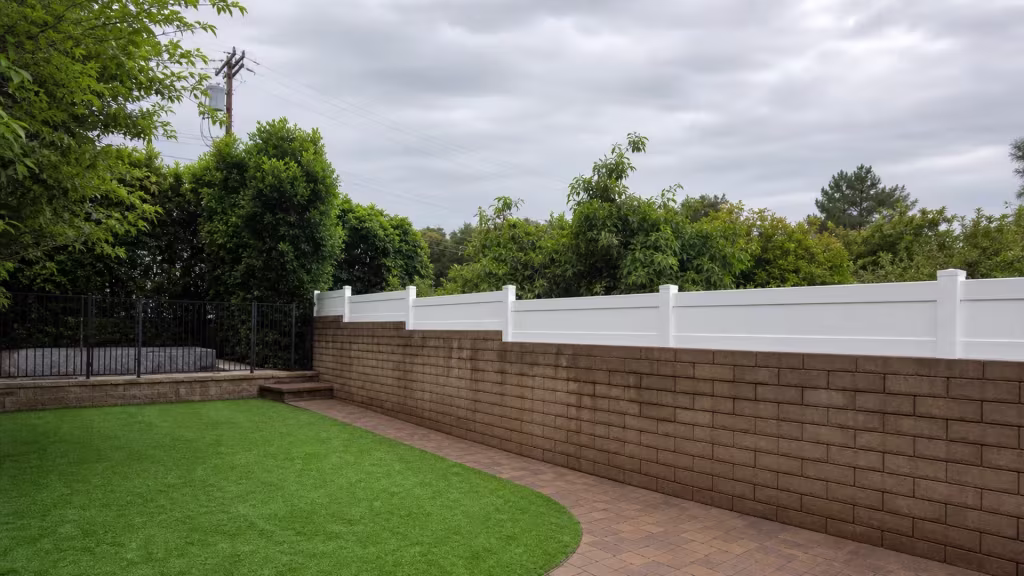A black metal gate and steps stand beside this stepped White vinyl privacy wall topper above a Sunland wall