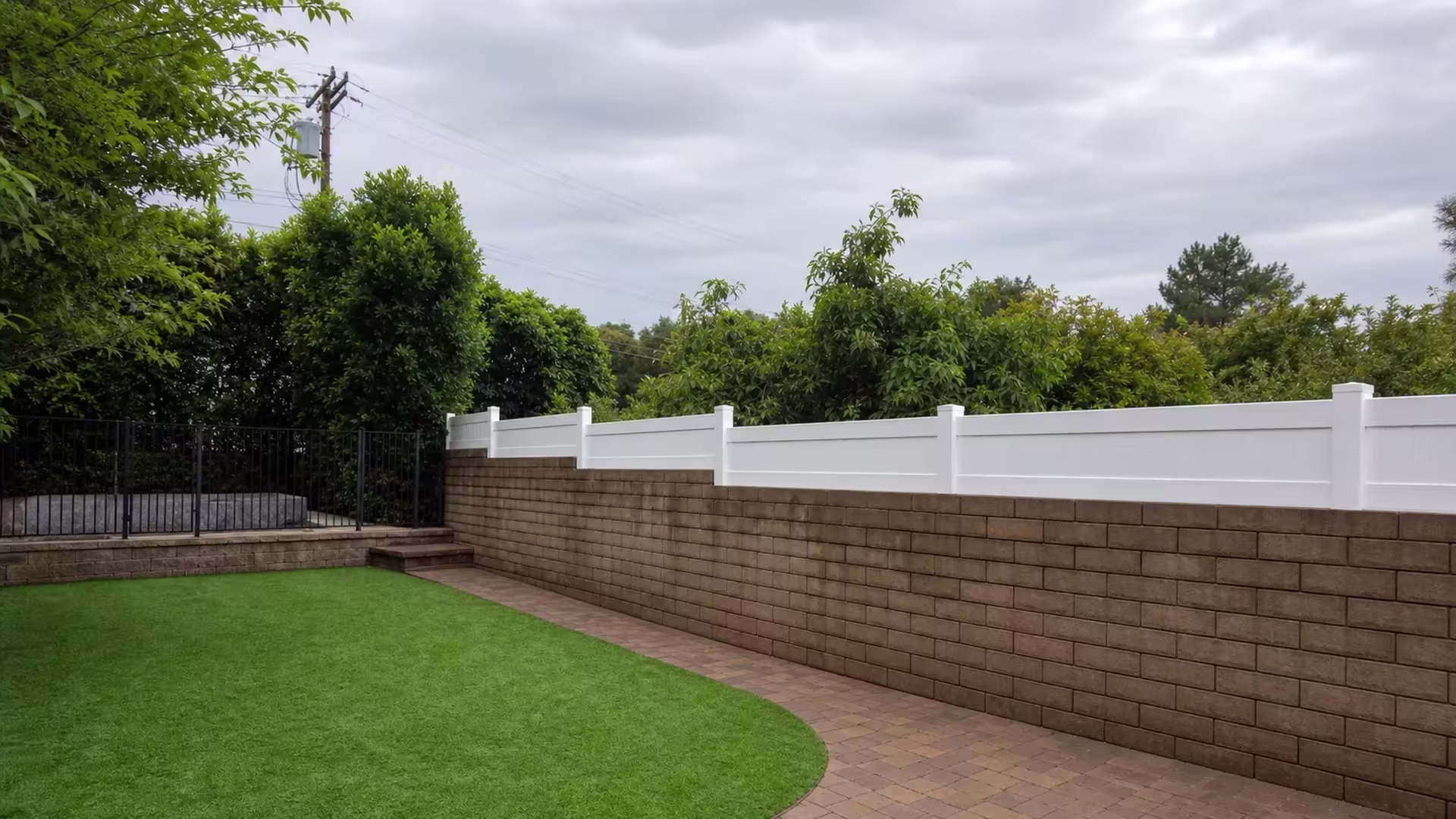 A black metal gate and steps stand beside this stepped White vinyl privacy wall topper above a Sunland wall