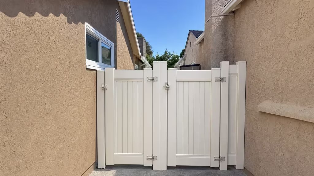 Rooflines and eaves from the adjoining house rise above this White vinyl gate on the Culver City privacy fence line
