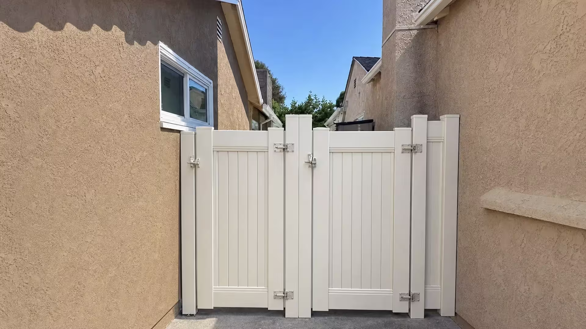 Rooflines and eaves from the adjoining house rise above this White vinyl gate on the Culver City privacy fence line
