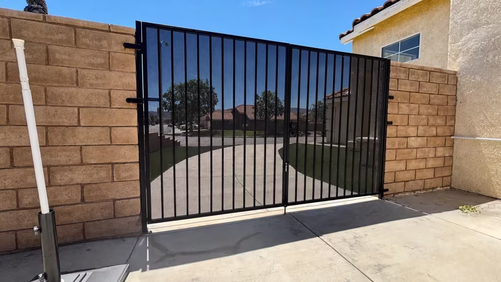 Before installation, a black metal mesh double gate spans a driveway between tan block walls.