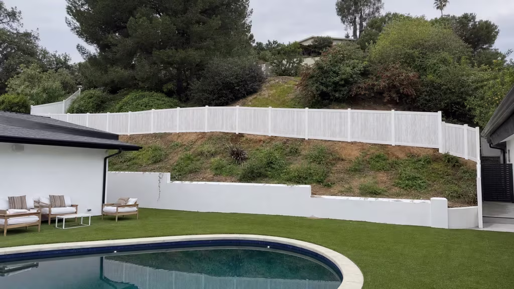 Exposed hillside soil and a distant palm rise beside this Aspen vinyl fence screening the pool area in Sherman Oaks