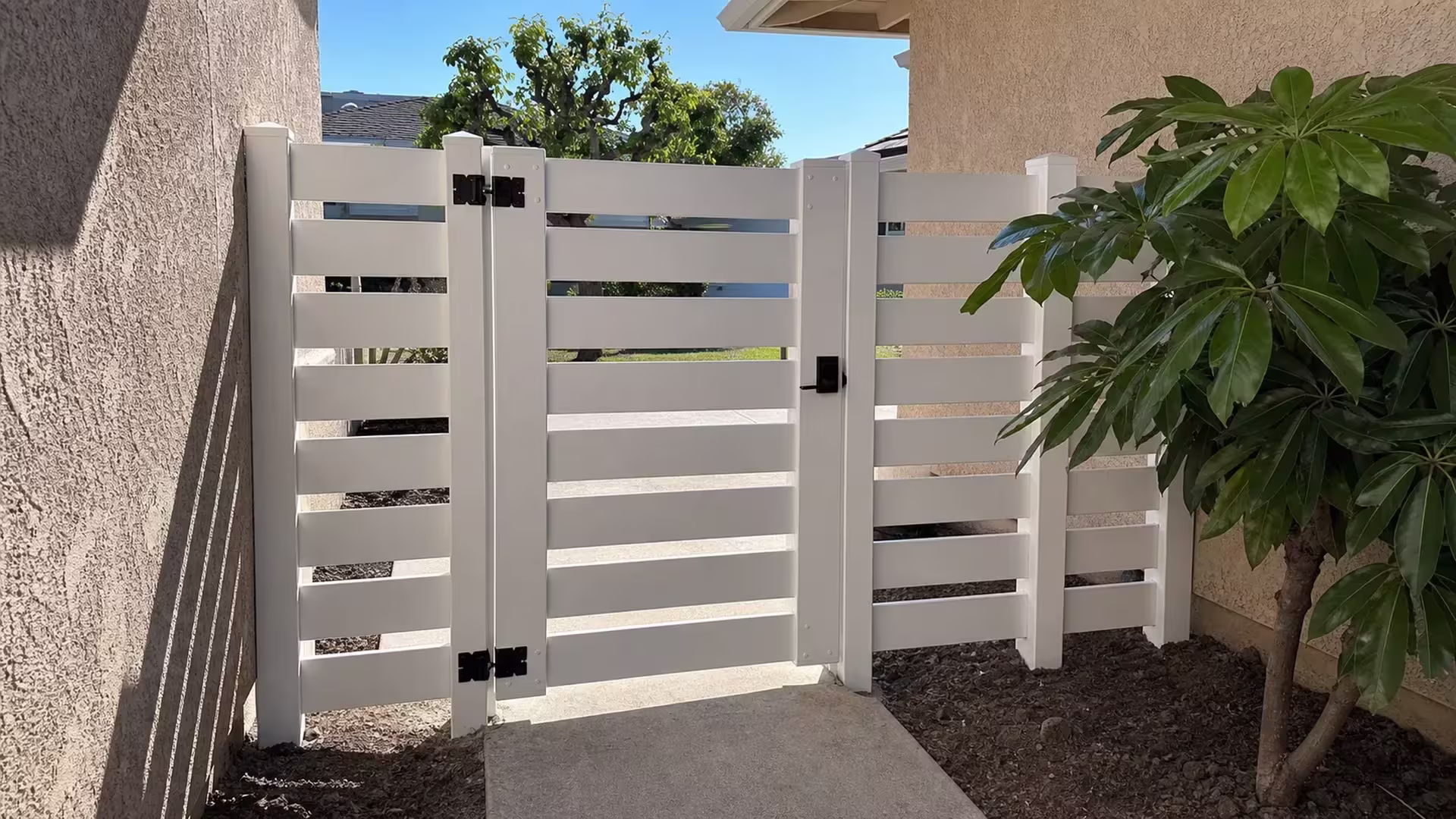 This White horizontal-picket vinyl fence and gate sit below stucco eaves and open sky in San Clemente