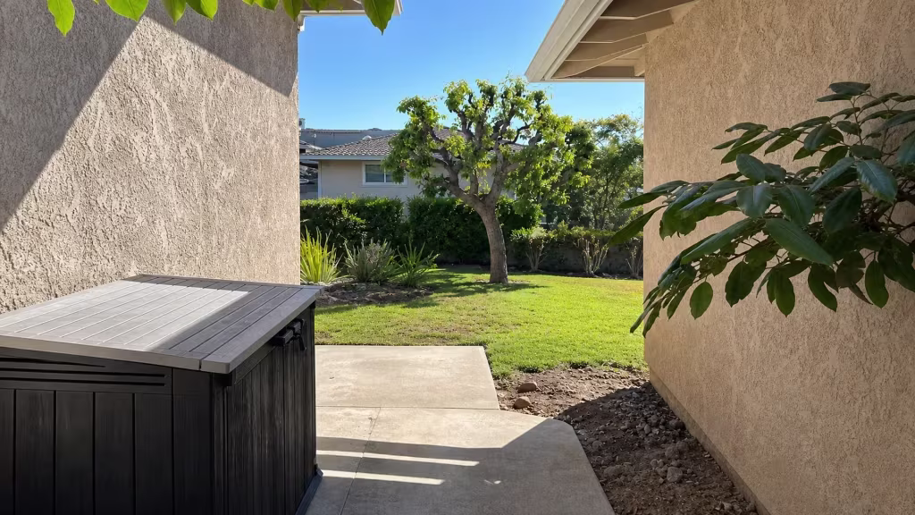 Before installation, an open passage between two stucco buildings leads to a landscaped lawn and trimmed trees.