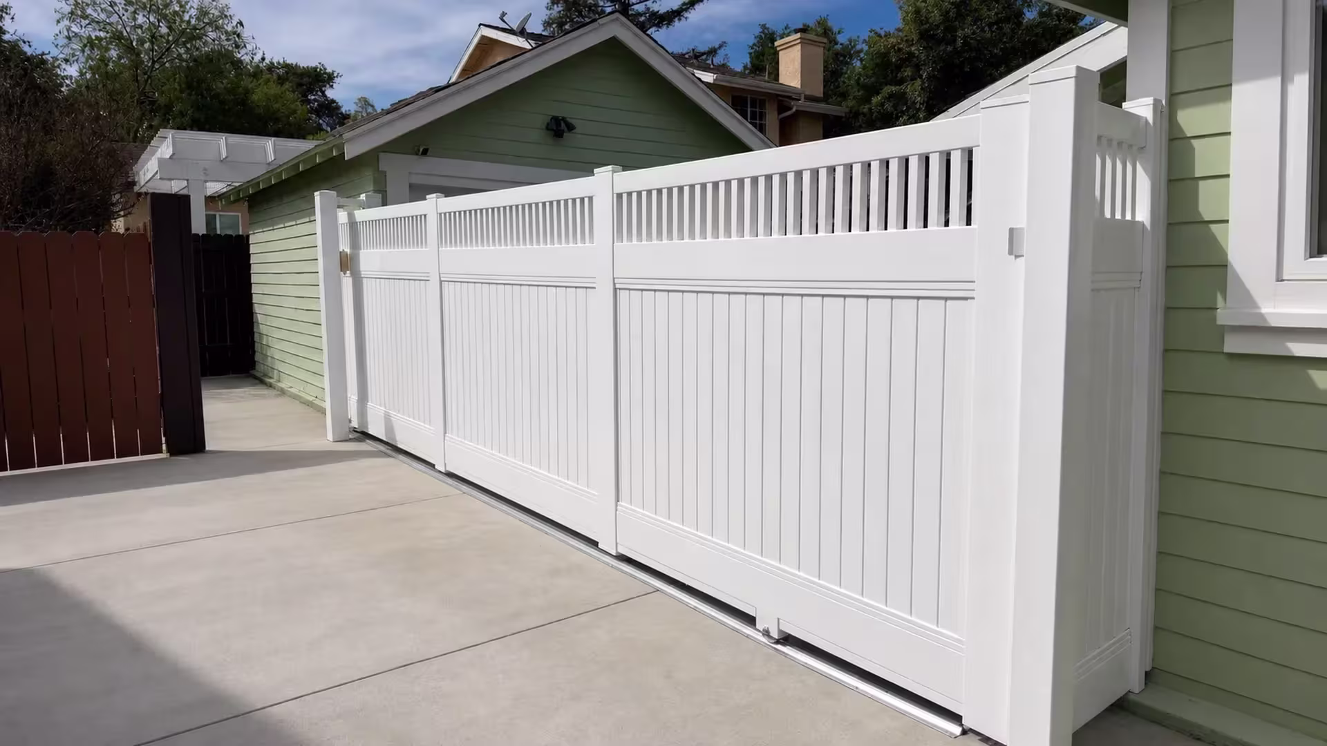 White vinyl fence encloses this Pasadena driveway for privacy, its top lined with pickets, in front of a pale green garage