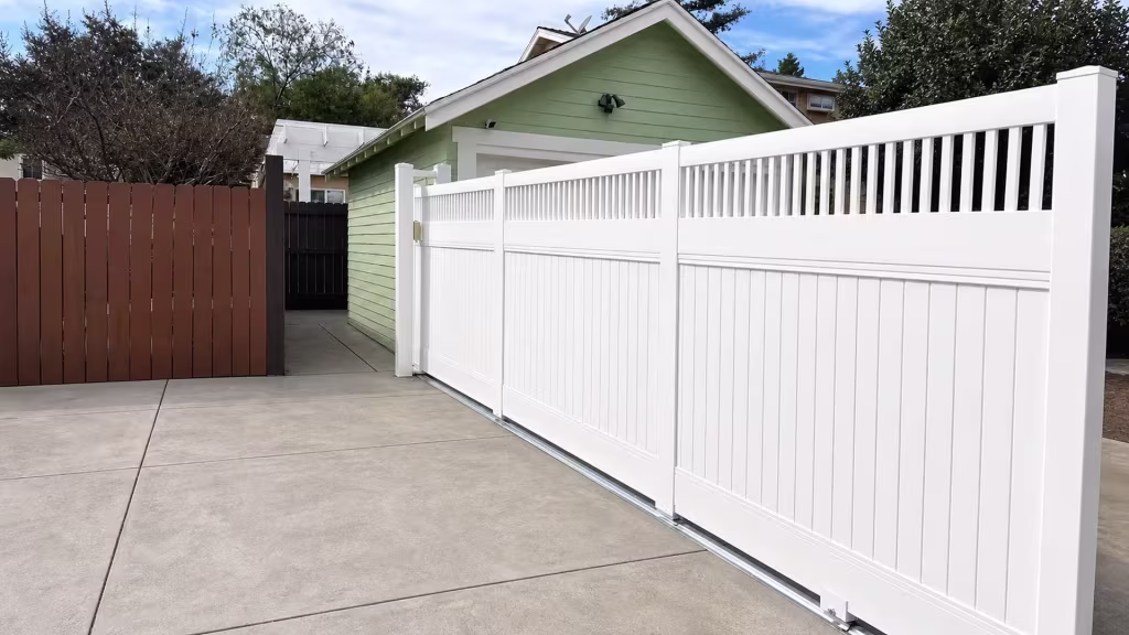 Picket-top White vinyl privacy fence running along a driveway beside a black fence and mature trees in Pasadena