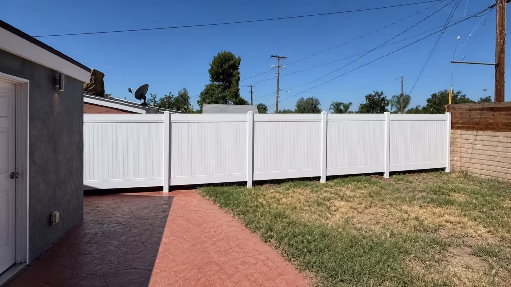 An exterior wall light and pale door trim mark the outbuilding beside this vinyl fence, finished in White, in Canyon Country