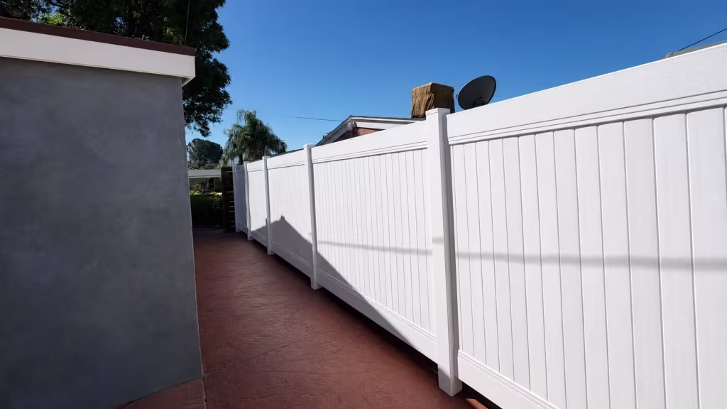 A red-brown stamped passage runs beside this White vinyl privacy fence beneath palm trees in Canyon Country